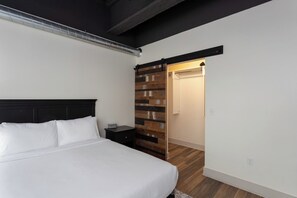 A bedroom with a bed, a nightstand, a wooden wall panel, and a sliding door leading to a bathroom. - Porsche Suite (Buffalo)