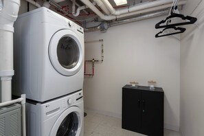A laundry room with stacked washing machines, a black cabinet, and visible plumbing.