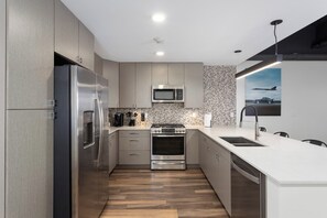 A modern kitchen with stainless steel appliances, a microwave, and a patterned backsplash.