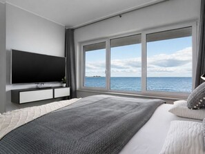 A modern bedroom with a large bed, a flat-screen TV, and a view of the sea. - Villa Blue Horizon (Kappeln)