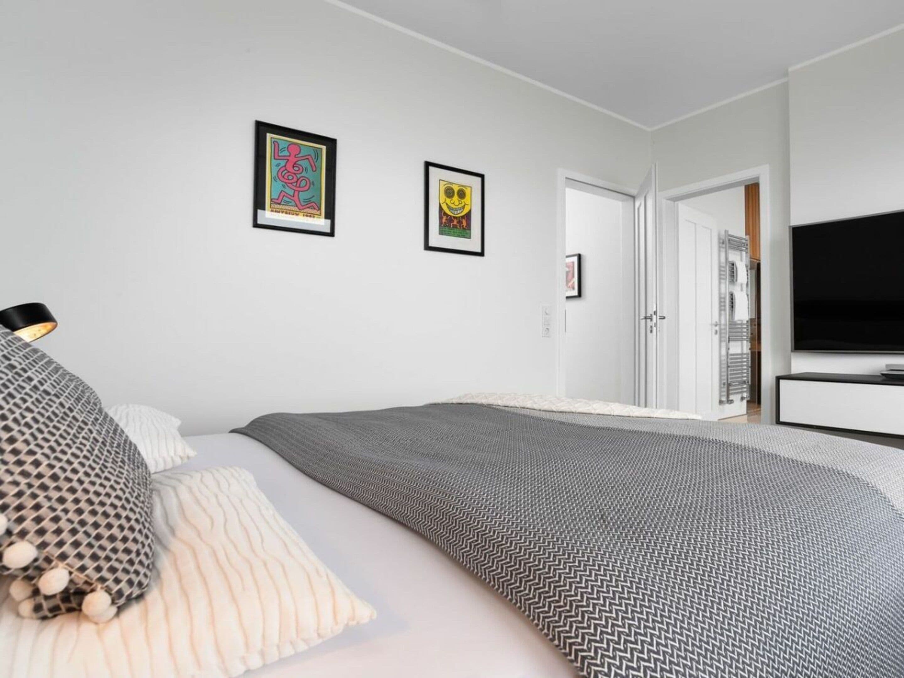 A modern bedroom with a bed, a TV, and two framed artworks on the wall.