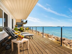 A wooden deck with lounge chairs and a table, overlooking a calm sea. - Villa Blue Horizon (Kappeln)