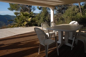 An outdoor patio with a wooden deck, white metal chairs, and a table. - Holiday Home With Pool and Natural View (Bagnols-en-Foret)