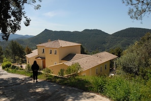 A two-story building with a tiled roof and a person walking on a dirt path. - Holiday Home With Pool and Natural View (Bagnols-en-Foret)