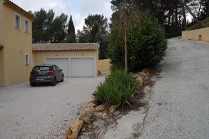 A residential driveway with a parked car, a garage, and a small garden area with plants. - Holiday Home With Pool and Natural View (Bagnols-en-Foret)