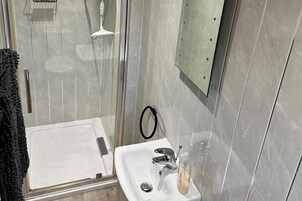 Un baño con ducha envuelta en vidrio, un lavamanos blanco con grifo cromado y un espejo en la pared.