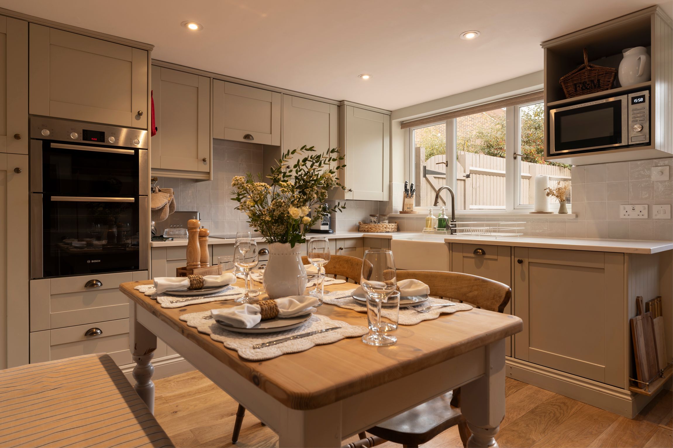 A modern kitchen with a dining area set for a meal, featuring stainless steel appliances, a wooden table, and a view of the outdoors.