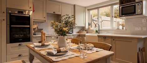 A modern kitchen with a dining area set for a meal, featuring stainless steel appliances, a wooden table, and a view of the outdoors.