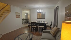 Un salon comprenant un canapé, une table basse en verre, une table à manger avec des chaises, un escalier et un tableau accroché au mur.