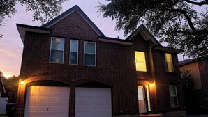 Une maison à deux étages, construite en briques, avec un garage, une porte d’entrée et un petit porche.