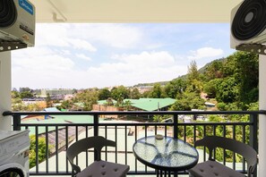 A balcony with two chairs and a table, overlooking a cityscape with buildings and greenery. - Kamala - Nature View from Above (Tambon Kamala)