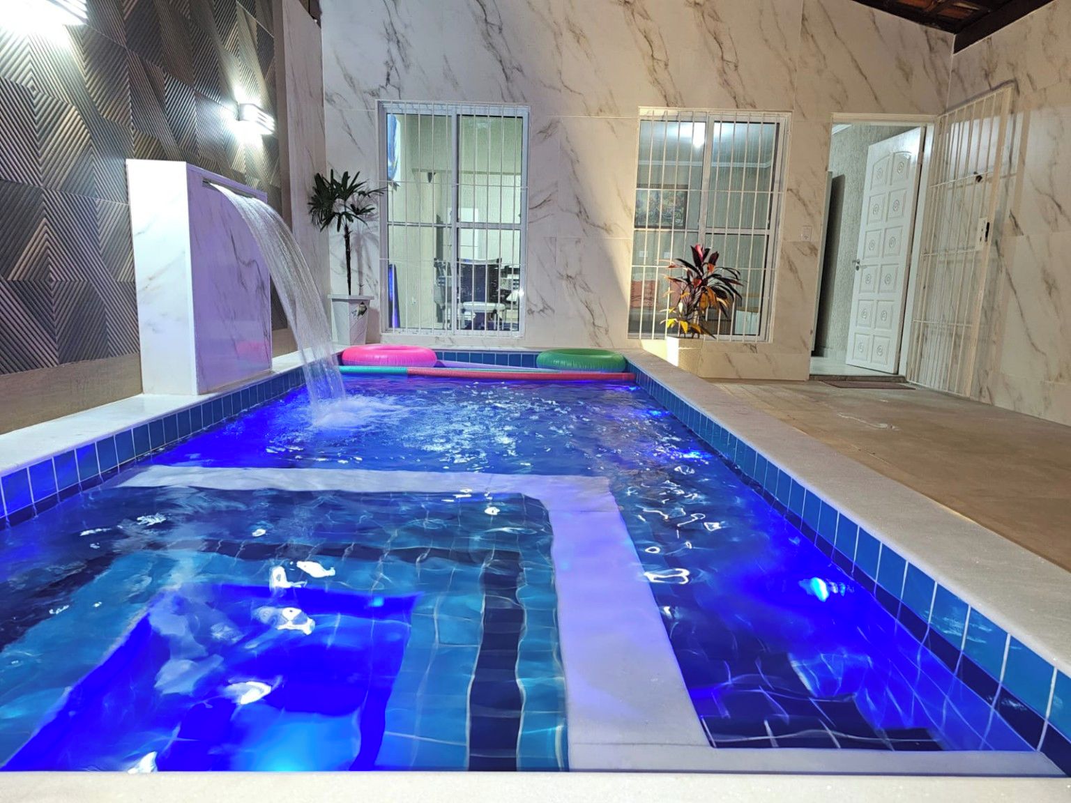 Une piscine intérieure avec un mur en marbre et une vue sur l’extérieur.