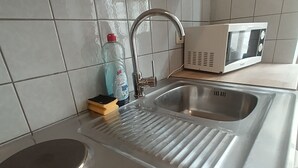 A kitchen with a stainless steel sink, a microwave, and a bottle of dish soap. - Cozy vacation rental near the harbor (Wismar)