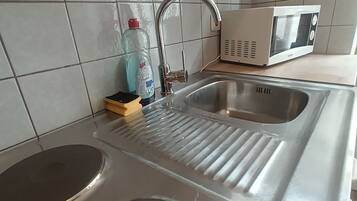 Una cocina con un lavamanos de acero inoxidable, un microondas y una botella de detergente.