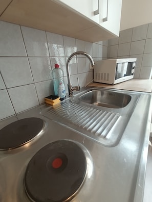 Eine Küche mit Spüle aus Edelstahl, einer Mikrowelle und einer Flasche Geschirrspülmittel.