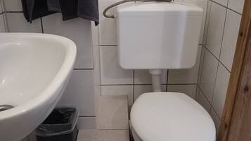 Een badkamer met een wit wastafel, toilet en een prullenbak.