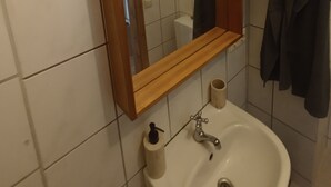 A bathroom with a wooden shelf, a mirror, a sink, and hanging towels. - Cozy vacation rental near the harbor (Wismar)