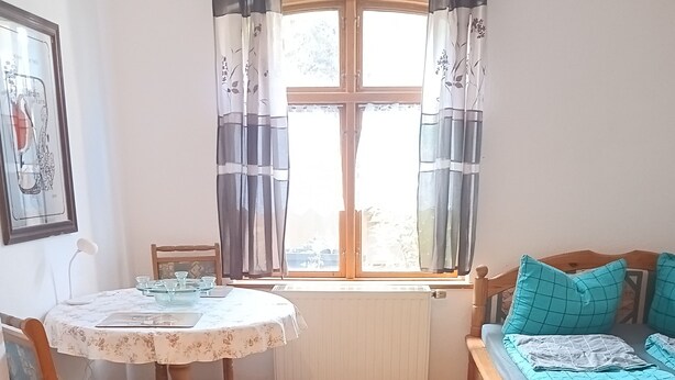 A room with a wooden floor, a round table with chairs, a bed with a blue bedspread, and a window with curtains. - Cozy vacation rental near the harbor (Wismar)
