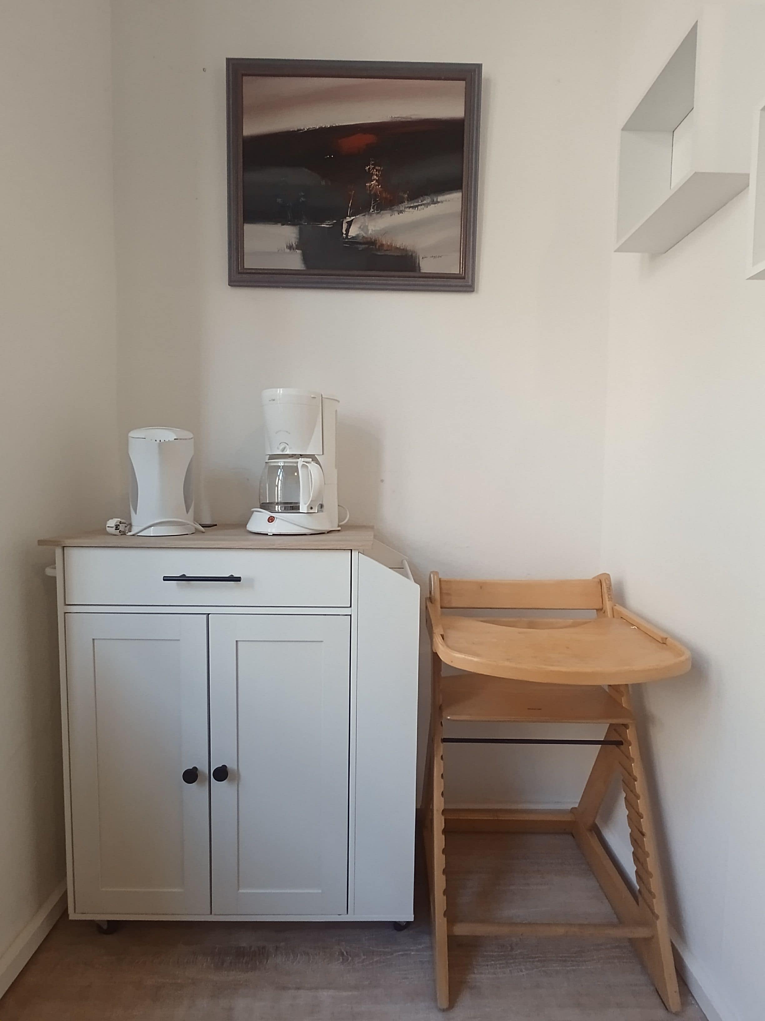 Een kitchenette met een koffiezetapparaat, een kast en een houten stoel.
