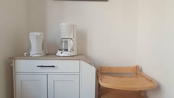 Een kitchenette met een koffiezetapparaat, een kast en een houten stoel.