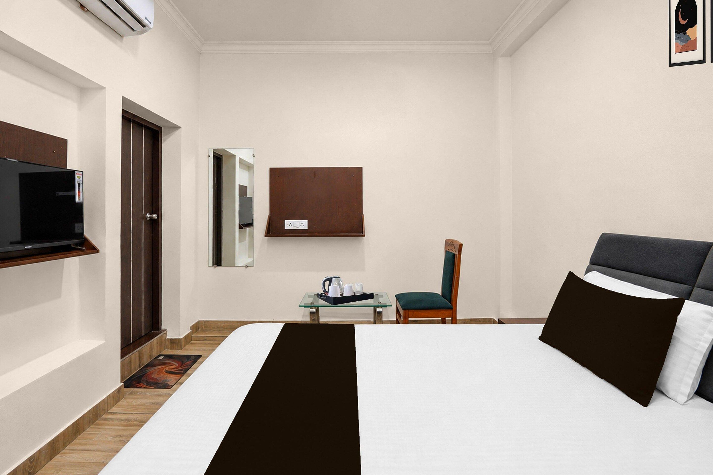 A hotel room with a bed, a television, a desk with a chair, and a wall-mounted mirror.
