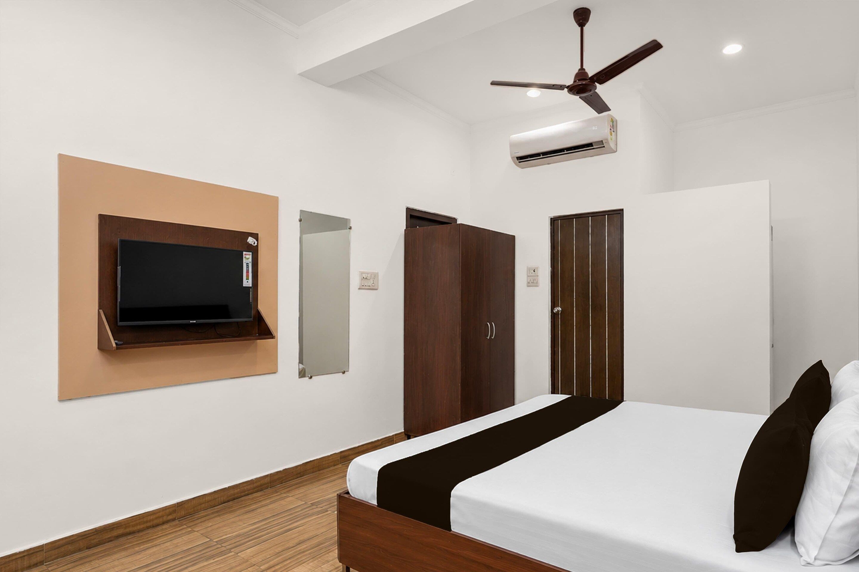 A bedroom with a bed, a television mounted on the wall, a wardrobe, and a ceiling fan.