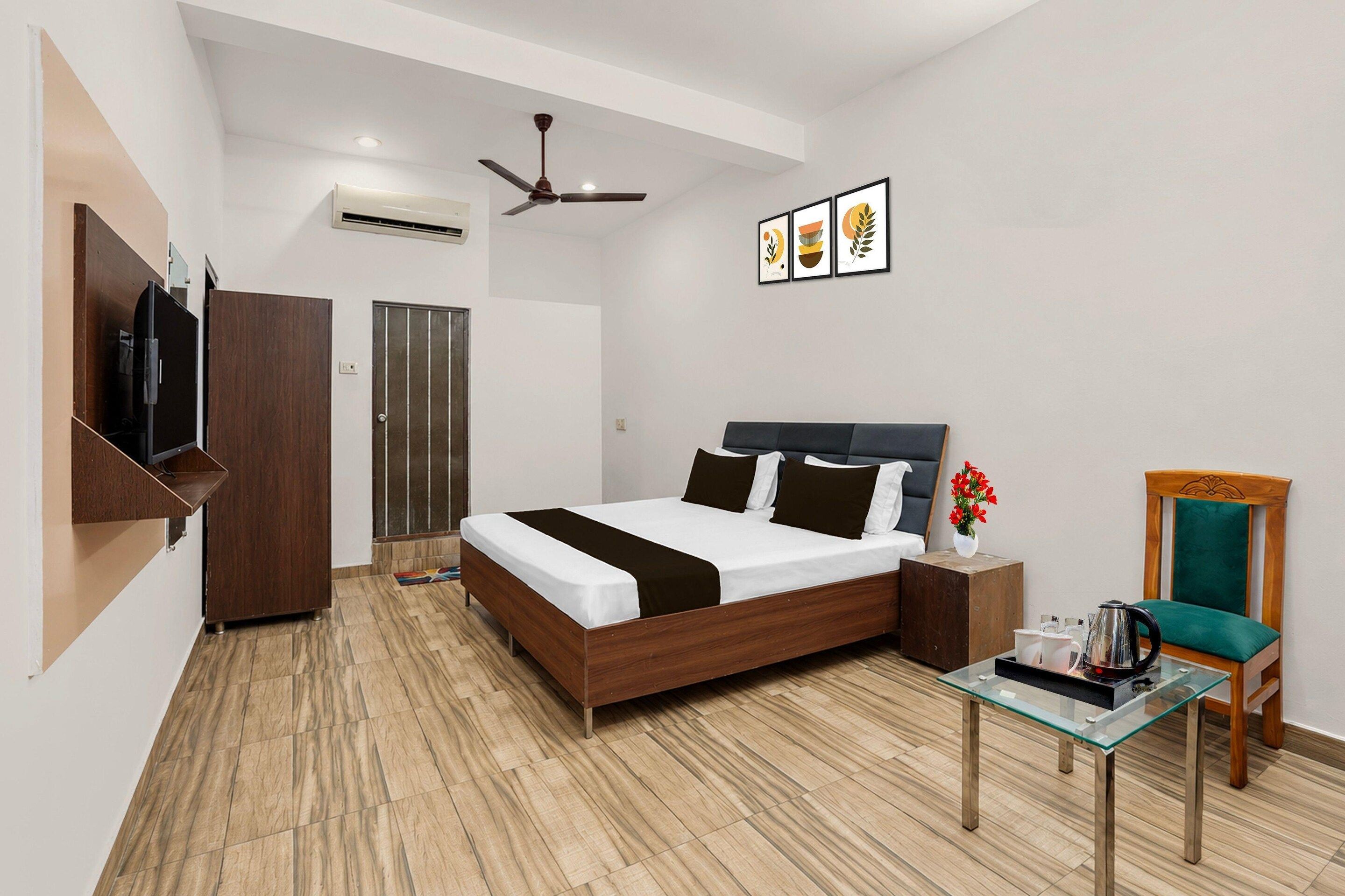 A modern hotel room with a bed, a TV, a ceiling fan, a coffee table, and a chair.