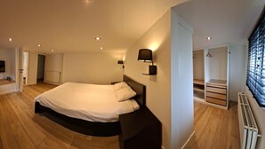 Un dormitorio con cama, lámparas de noche, televisor y radiador.