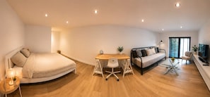 Een moderne, open woonruimte met een bed, bank, eettafel en een televisie.
