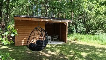 Une structure en bois avec une chaise suspendue et une table, le tout entouré de verdure.