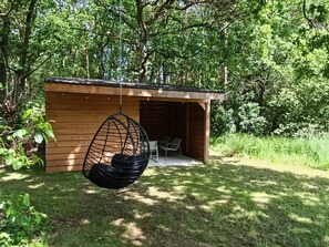 A wooden structure with a hanging chair and a table, surrounded by greenery.