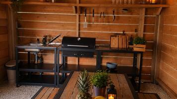 L’intérieur est en bois, avec une table à manger placée au centre, entourée de bancs en bois, d’un barbecue et de divers ustensiles de cuisine accrochés au mur.