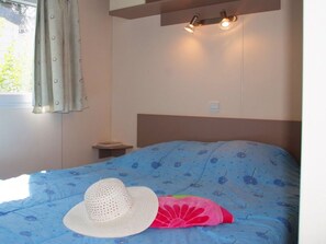 A bedroom with a bed, a nightstand, a window with curtains, and a wall-mounted light fixture. - Relaxed Seaside Escape in France (Hyères)