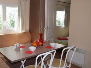 A dining area with a table set for two, a red vase, and fruit on the table. - Relaxed Seaside Escape in France (Hyères)
