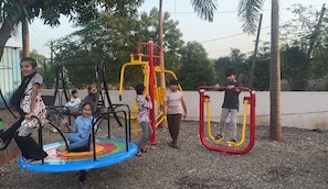 A playground with swings, a merry-go-round, and exercise equipment. - Rushi Resort By ARDEA (Valsad)