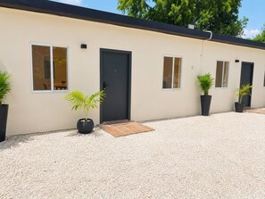 A modern building with a beige facade, black doors, and windows. There are potted plants and a gravel driveway. - Charming Curaçao – Central, Private & Free Parking (Willemstad)