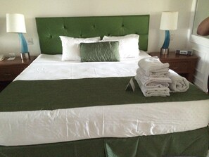 Ein ordentlich bezogenes Bett mit einer grünen Tagesdecke, weißen Bettwäsche und einem Stapel Handtüchern an der Seite.