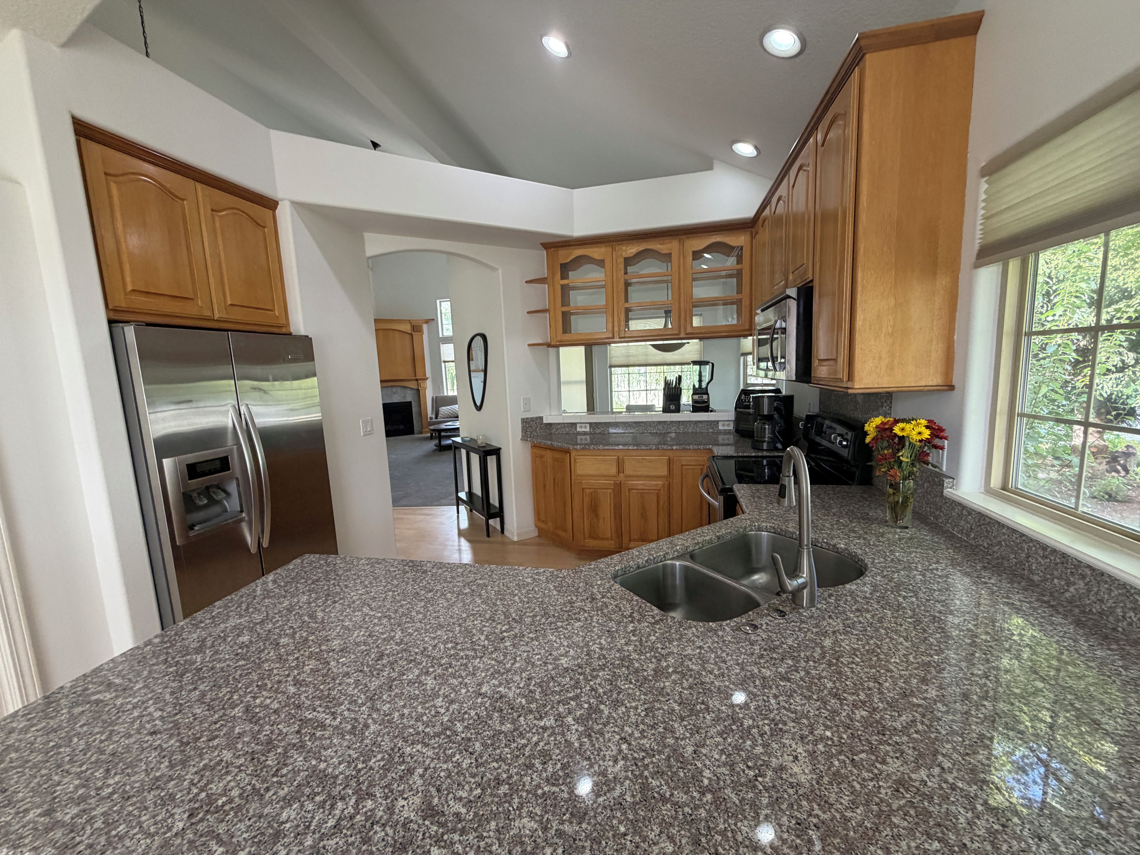 A kitchen with granite countertops, stainless steel appliances, wooden cabinets, and a large window.