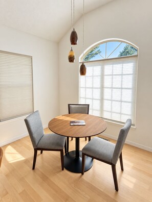 A dining area with a round table, four grey upholstered chairs, and pendant lighting. - Close to Lakeview Golf Course (Meridian)