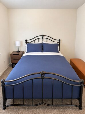 Ein Bett mit Metallgestell, ein Nachttisch mit Lampe und eine Bank.