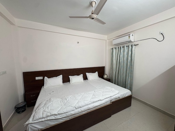 A bedroom with a bed, a ceiling fan, an air conditioning unit, and a curtain.
