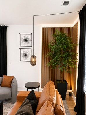 Ein modernes Wohnzimmer mit einer Ledersofa, einem kleinen runden Tisch und einer Topfpflanze.