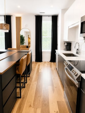A modern kitchen with a wooden floor, a built-in oven, a coffee maker, and a large window with curtains. - Ivory Oasis, 85" TV, Walkable with Free Parking and a Patio (Atlanta)