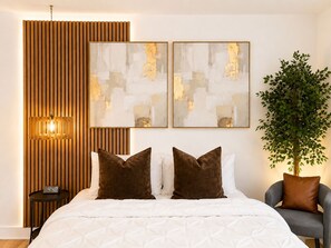 Ein Schlafzimmer mit einem Bett, zwei Kissen, einem Nachttisch mit einer Uhr, einer Wandleuchte und zwei abstrakten Gemälden.