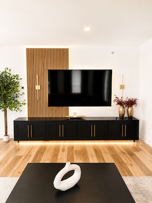 Ein modernes Wohnzimmer mit einer schwarzen Unterhaltungseinheit, einem großen Flachbildfernseher und einer einzigartigen weißen Skulptur auf einem schwarzen Tisch.