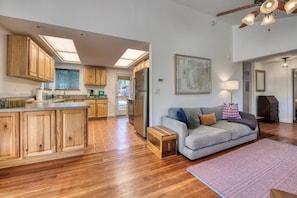 A modern kitchen with wooden cabinets, a central island, and a dining area with a sofa and a rug. - Cozy house on seven wooded acres near Hamilton (Hamilton)