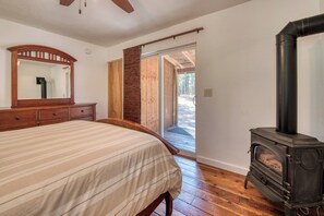 A bedroom with a bed, dresser, mirror, and a wood-burning stove. - Cozy house on seven wooded acres near Hamilton (Hamilton)