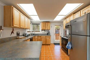 Une cuisine avec des meubles en bois, un réfrigérateur en acier inoxydable, une cuisinière à gaz et un puits de lumière.