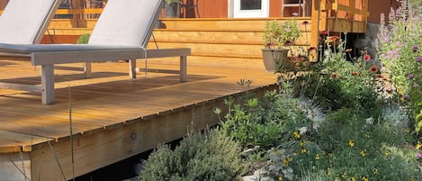 A wooden cabin with a deck, lounge chairs, and a stone garden.