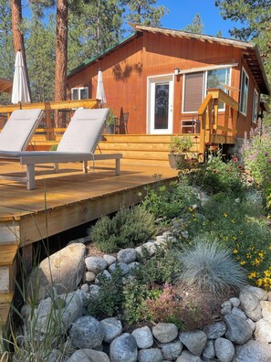 A wooden cabin with a deck, lounge chairs, and a stone garden. - Cozy house on seven wooded acres near Hamilton (Hamilton)